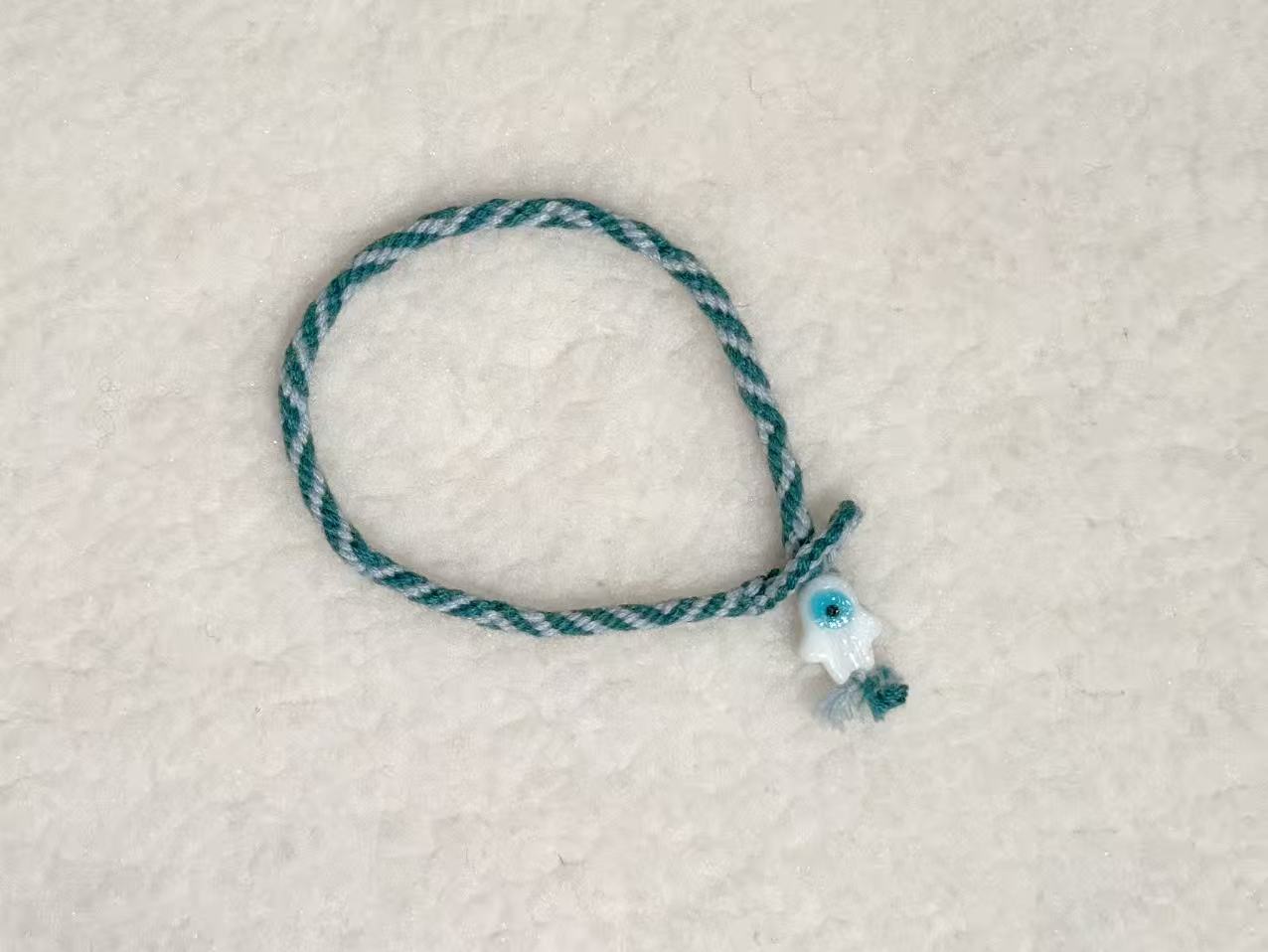 Evil Eye E12 — Teal braid · Pale charm